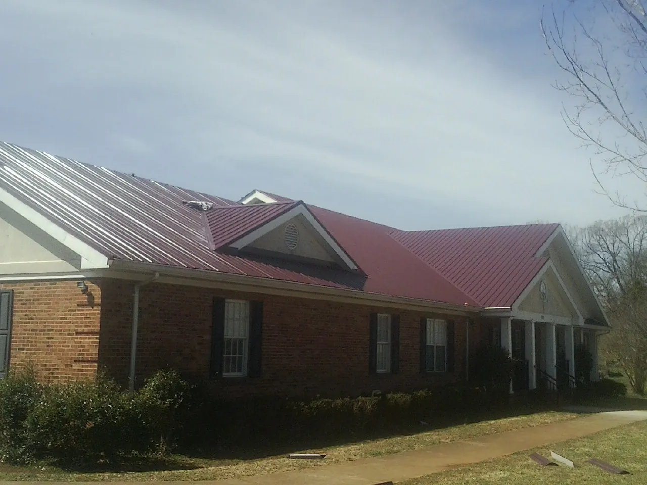 Red metal roof with gabled entries on a long brick building, from a Hail Damage Roof Repair job in Williamstown